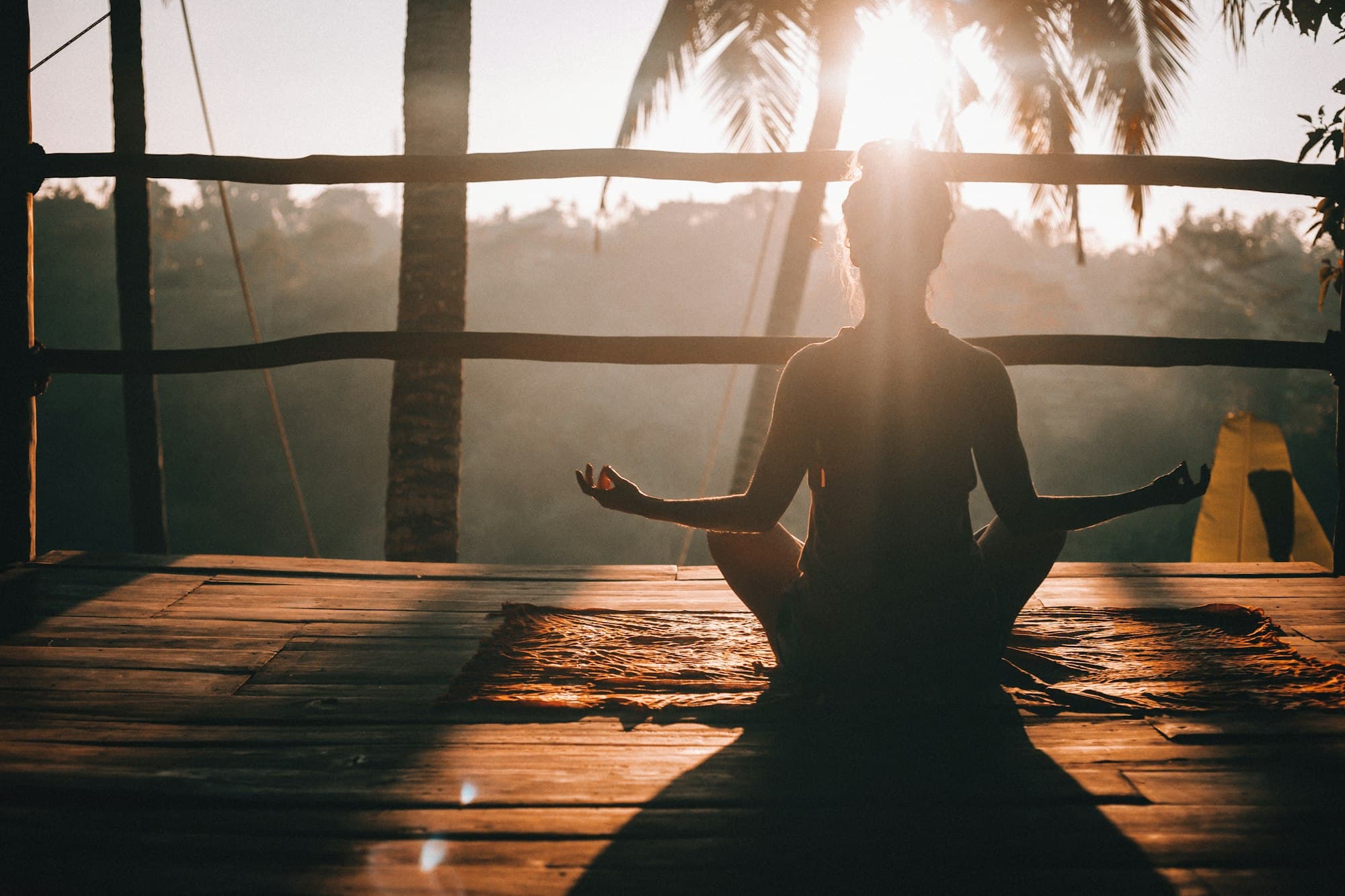 A person meditating on a wooden deck as the sun rises
