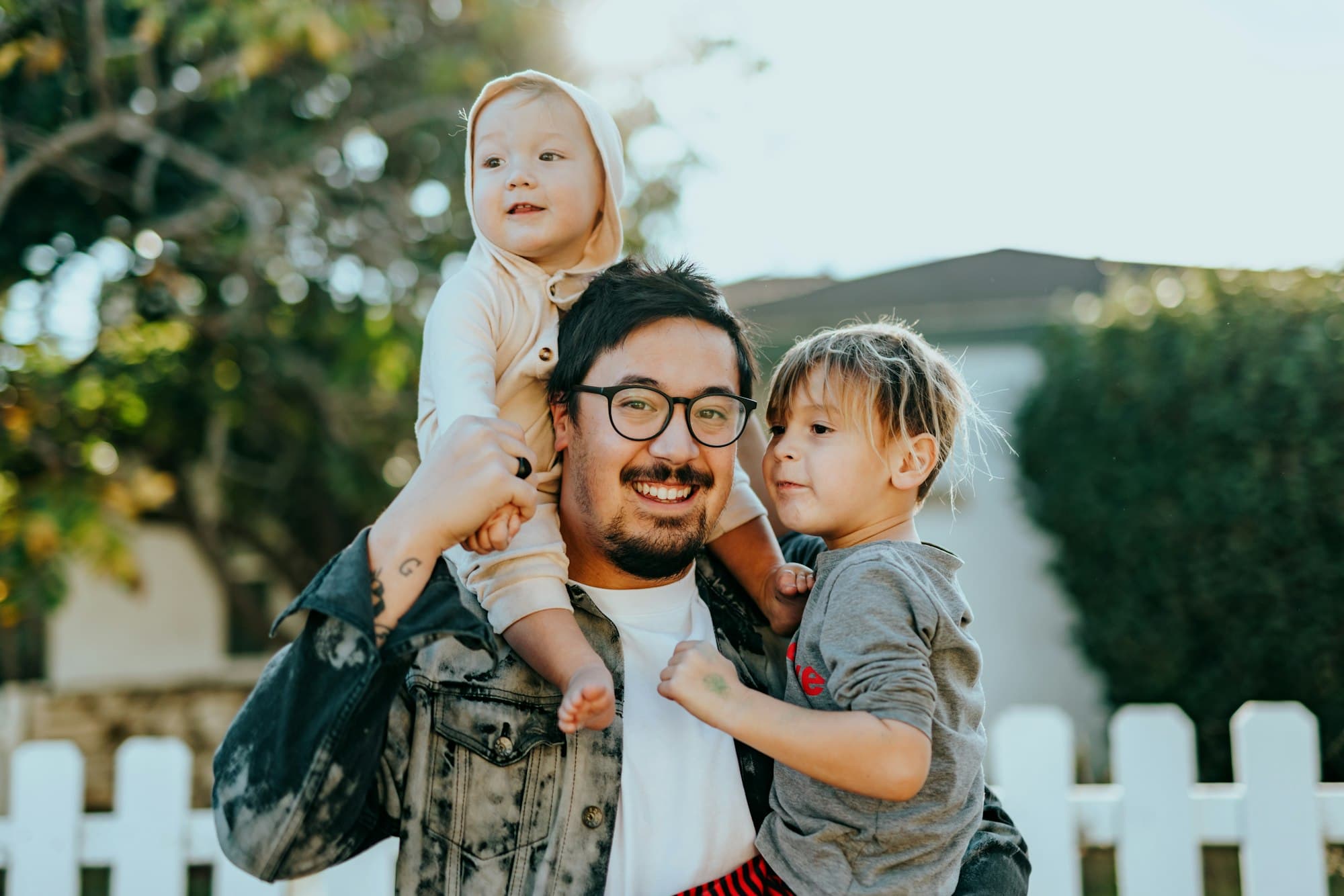 A smiling father holding his two young children outdoors